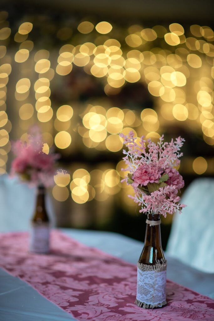 Tender fragrant pink flowers in decoupage bottles placed on banquet table in fine restaurant against blurred garlands